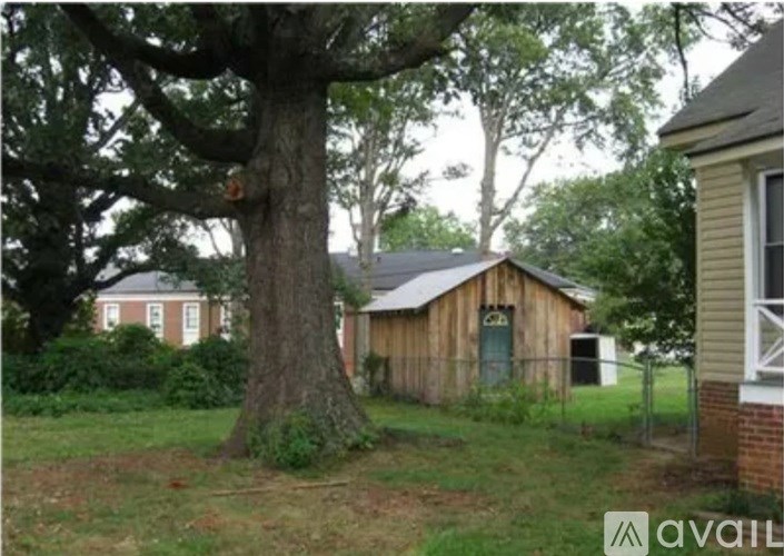 A tree in front of a white house with a shed in the background.