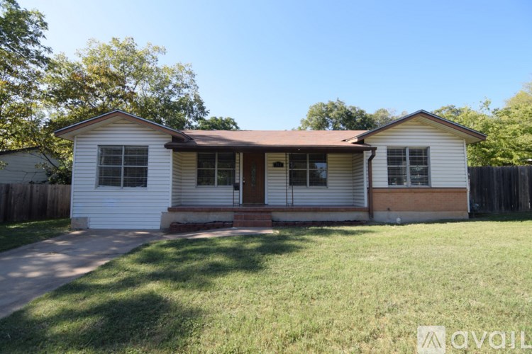 A house with a brown roof and white walls is surrounded by a green lawn.