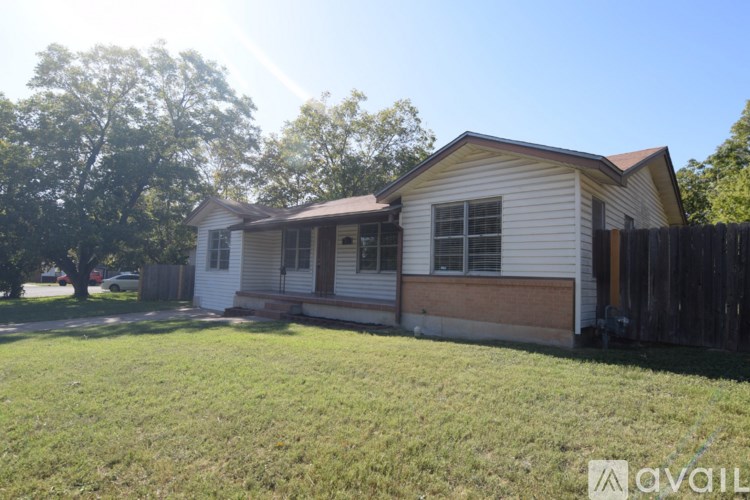 A house with a white siding and a brown roof is surrounded by a grassy lawn and a wooden fence.