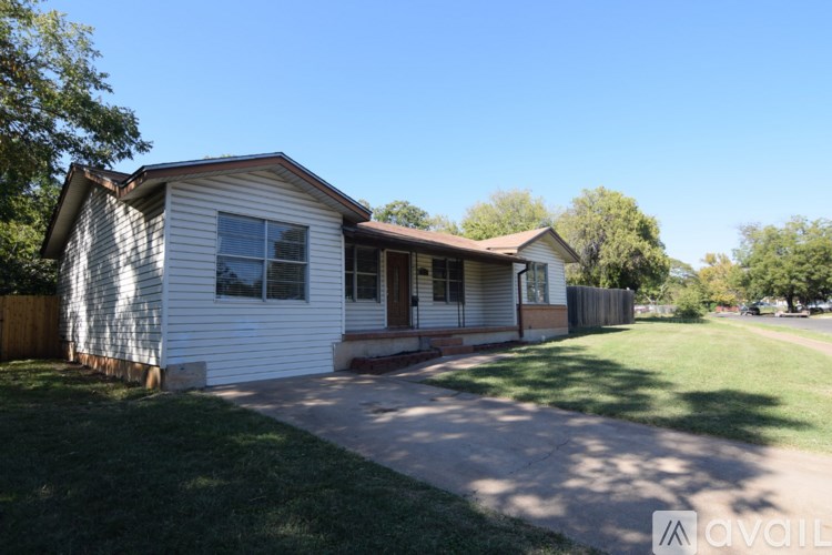 A house with a white siding and a brown roof is surrounded by a green lawn.