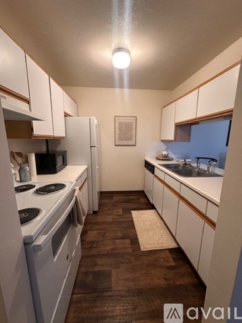 A kitchen with white appliances and wooden floors.