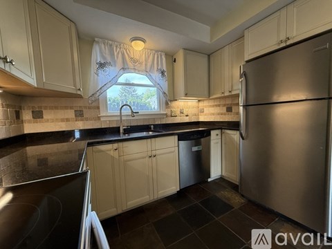A kitchen with a stainless steel refrigerator and a window with a view of trees.