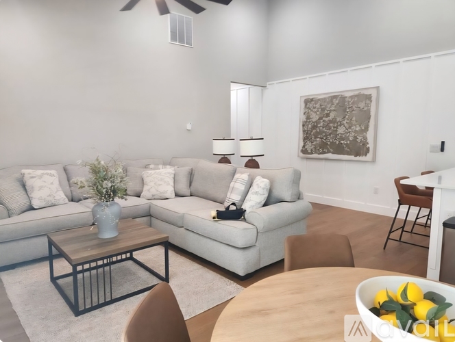 A spacious living room with a kitchen in the background, furnished with a white sofa, chairs, and a coffee table.