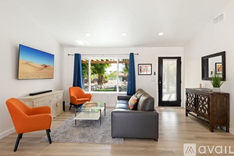 A living room with a large painting of a desert scene on the wall and a view of the outdoors through the window.
