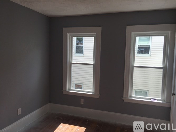 Two windows with white blinds in a room with grey walls.