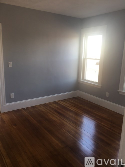 A room with wooden floors and a window letting in sunlight.