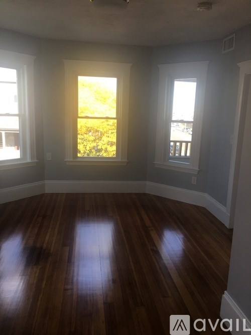 A room with wooden floors and two windows letting in sunlight.