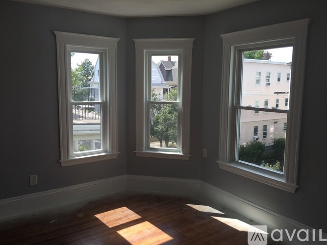 Three windows in a room with wooden floors and walls painted in a light grey color.
