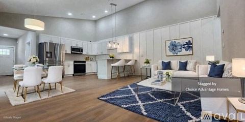 A spacious living room with a kitchen in the background, furnished with a white sofa, chairs, and a coffee table.