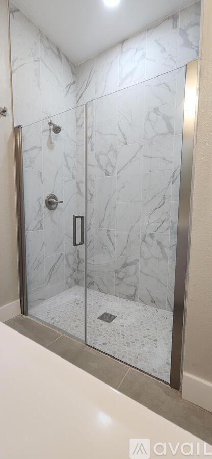 A bathroom with a marble wall and a glass shower door.