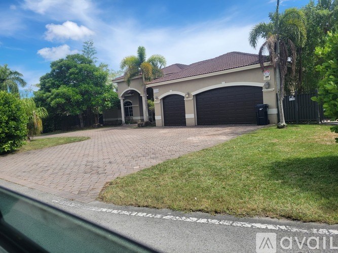 A house with a driveway and garage doors is surrounded by greenery.