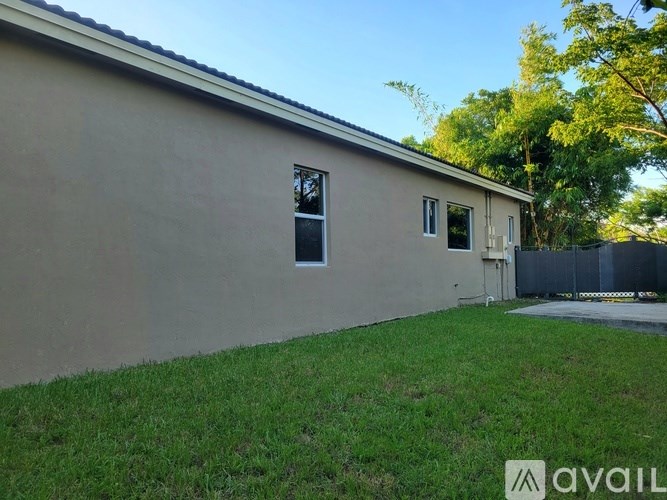 A beige house with a brown roof, a green lawn, and a fence.