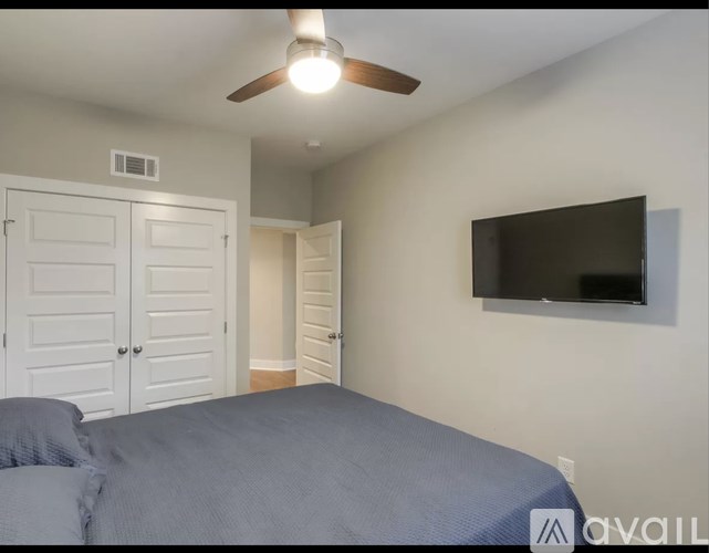 A bedroom with a bed, a ceiling fan, and a flat-screen TV mounted on the wall.