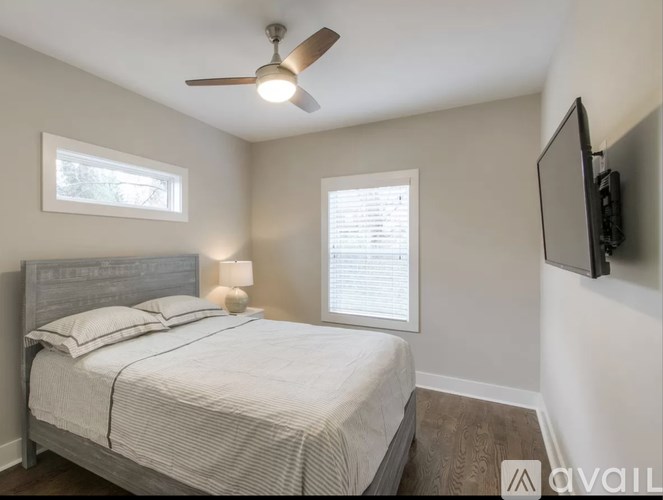 A bedroom with a bed, a ceiling fan, and a flat-screen TV mounted on the wall.