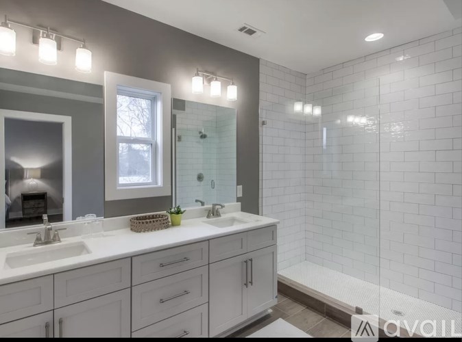 A bathroom with a white tiled shower and a large mirror above the sink.