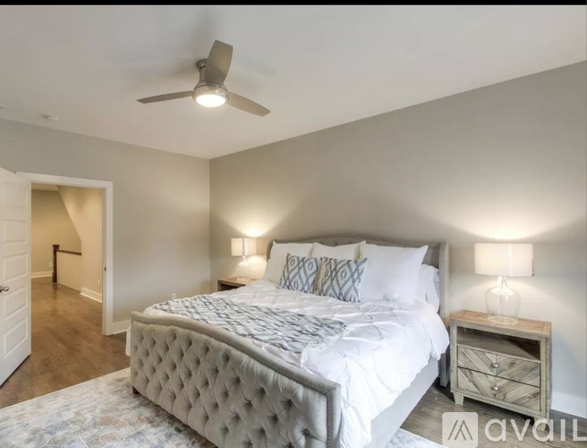 A bedroom with a large bed, a ceiling fan, and a nightstand with a lamp.