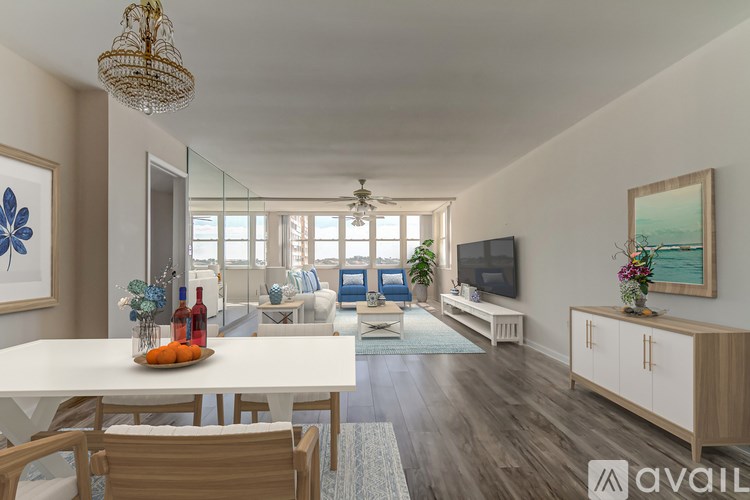 A well-lit, spacious living room with a dining table and chairs, a sofa, a television, and a view of the outdoors through the windows.