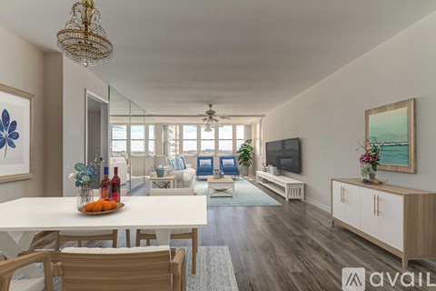 A well-lit, spacious living room with a dining table and chairs, a sofa, a television, and a view of the outdoors through the windows.