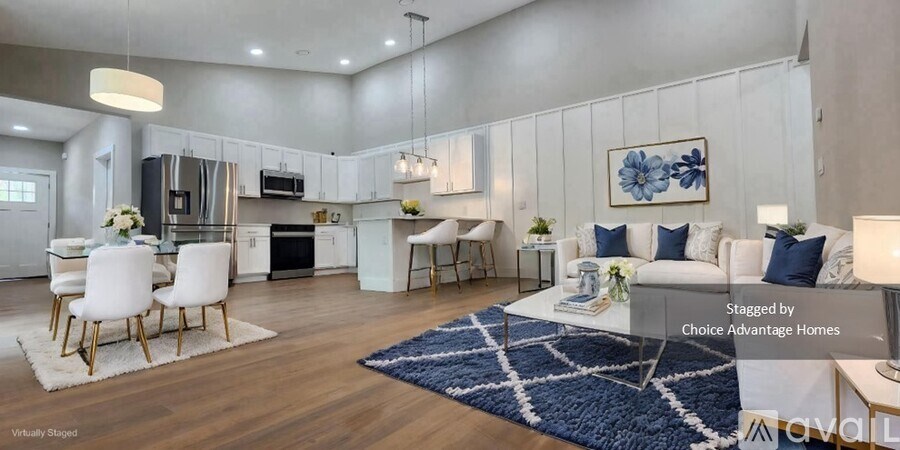 A spacious living room with a kitchen in the background, furnished with a white sofa, chairs, and a coffee table.