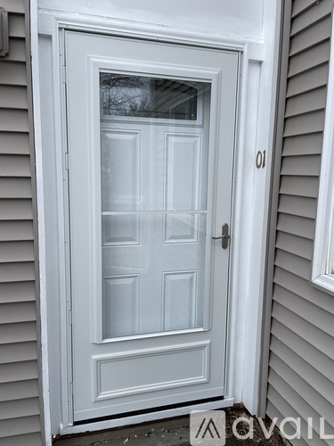 A white door with a glass window and a handle is set in a grey wall.