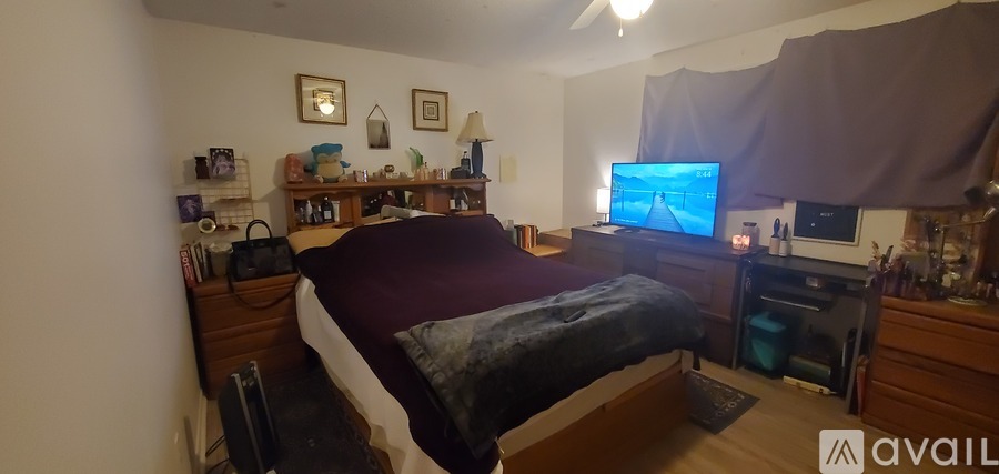 A bedroom with a bed, a desk with a computer, and a TV on the wall.