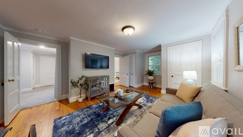 A living room with a blue rug and a television on the wall.