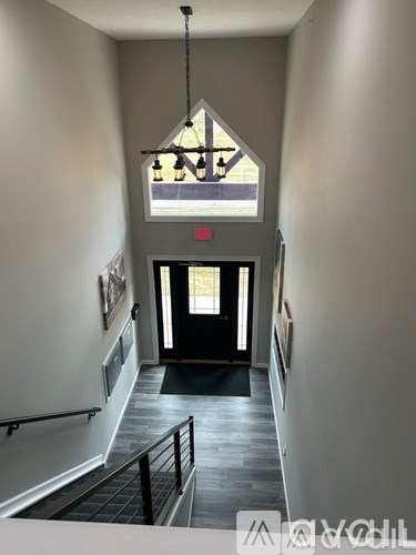 A hallway with a black door and a chandelier hanging from the ceiling.