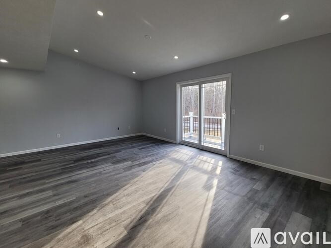 A spacious room with wooden flooring and a sliding glass door.