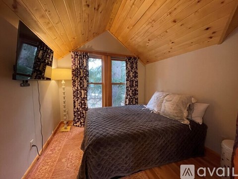 A bedroom with a bed, a window with curtains, and a wooden ceiling.