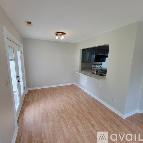 A room with wooden flooring and a window overlooking a kitchen.