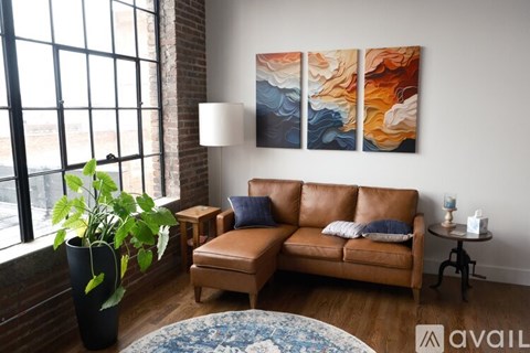 A living room with a brown leather couch, a round rug, and a large abstract painting on the wall.