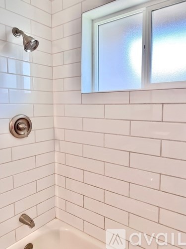 A white tiled bathroom with a tub, shower, and window.