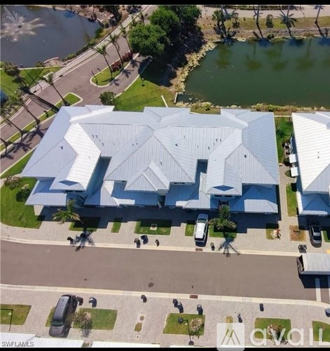 A large white building with a triangular roof is surrounded by a grassy area and a body of water.
