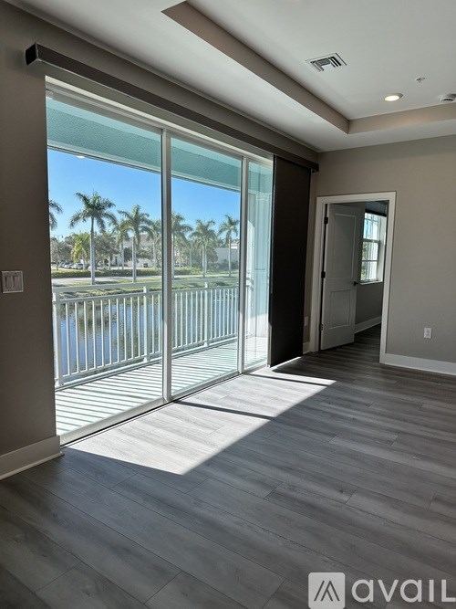 A room with a sliding glass door leading to a balcony with a view of a pool and palm trees.