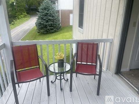 Two red chairs on a wooden deck with a glass table between them.