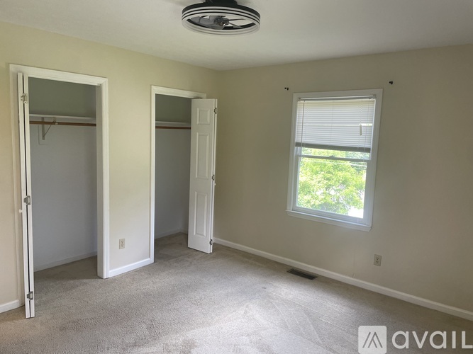 A room with a carpeted floor, two open doors, and a window with blinds.