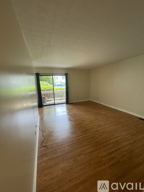 A room with wooden floors and a window overlooking a fence.