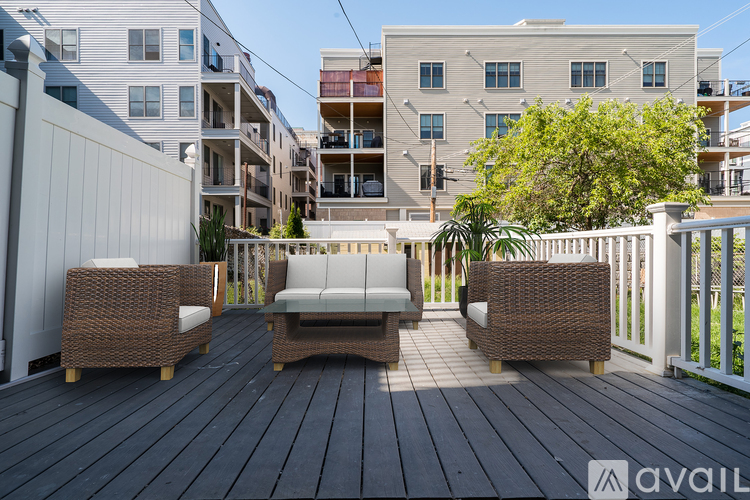 A wooden deck with a sofa and chairs is in front of apartment buildings.