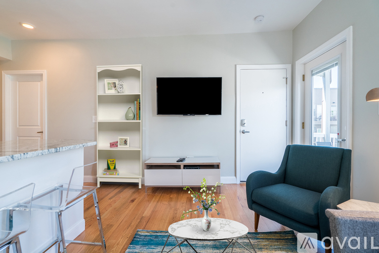 A living room with a grey sofa, a white coffee table, a television, and a white shelf with books and decorations.