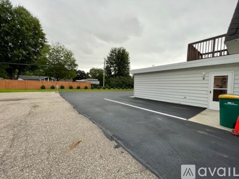 A gravel parking lot with a white building and a green trash can.