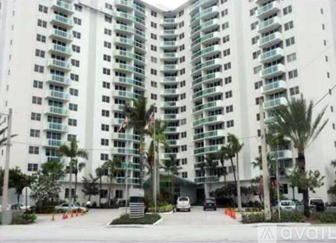 A large white building with balconies and palm trees in front.