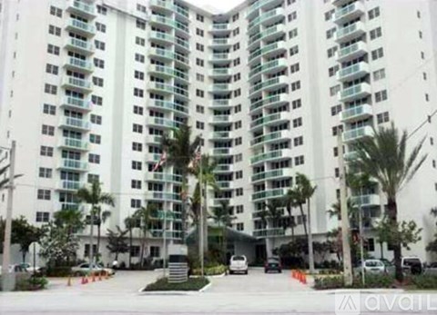 A large white building with balconies and palm trees in front.