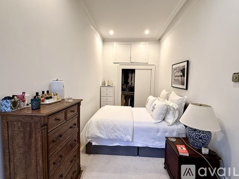 A well-lit bedroom with a large bed, a wooden dresser, and a nightstand with a lamp.