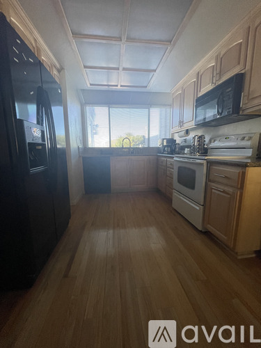A kitchen with wooden floors and a black fridge.