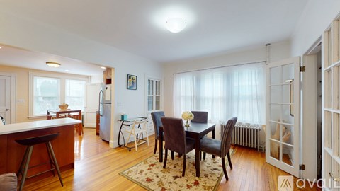 A dining room with a table set for two and a kitchen area with a refrigerator.