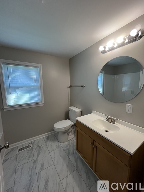 A bathroom with a toilet, sink, mirror, and lights.