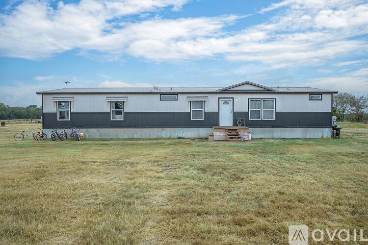 A grey and white mobile home sits in a grassy field with a blue sky above.