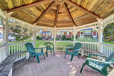 A wooden gazebo with green chairs and a bench.