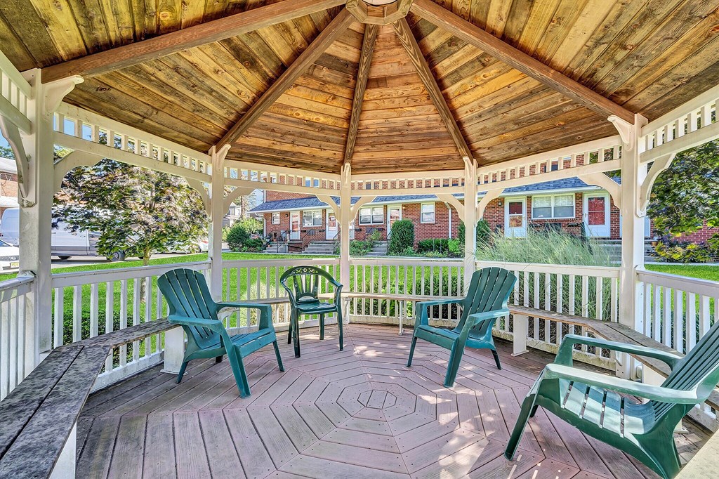 A wooden gazebo with green chairs and a bench.
