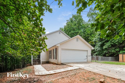 A house with a garage is surrounded by trees and has a FirstKey Homes sign.